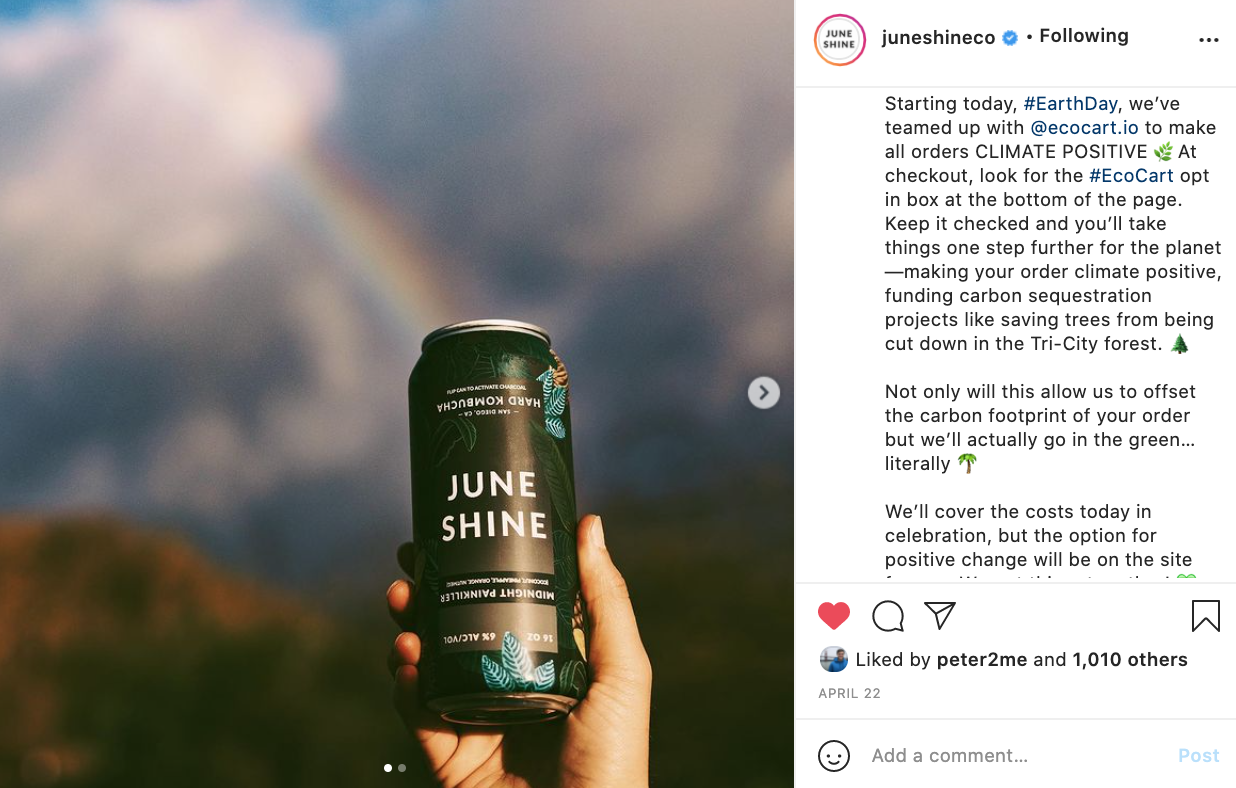 A can of JuneShine Hard Kombucha is being held up in front of a rainbow.